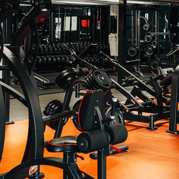 Krachtzone met dumbbells en krachtapparaten op een oranje vloer